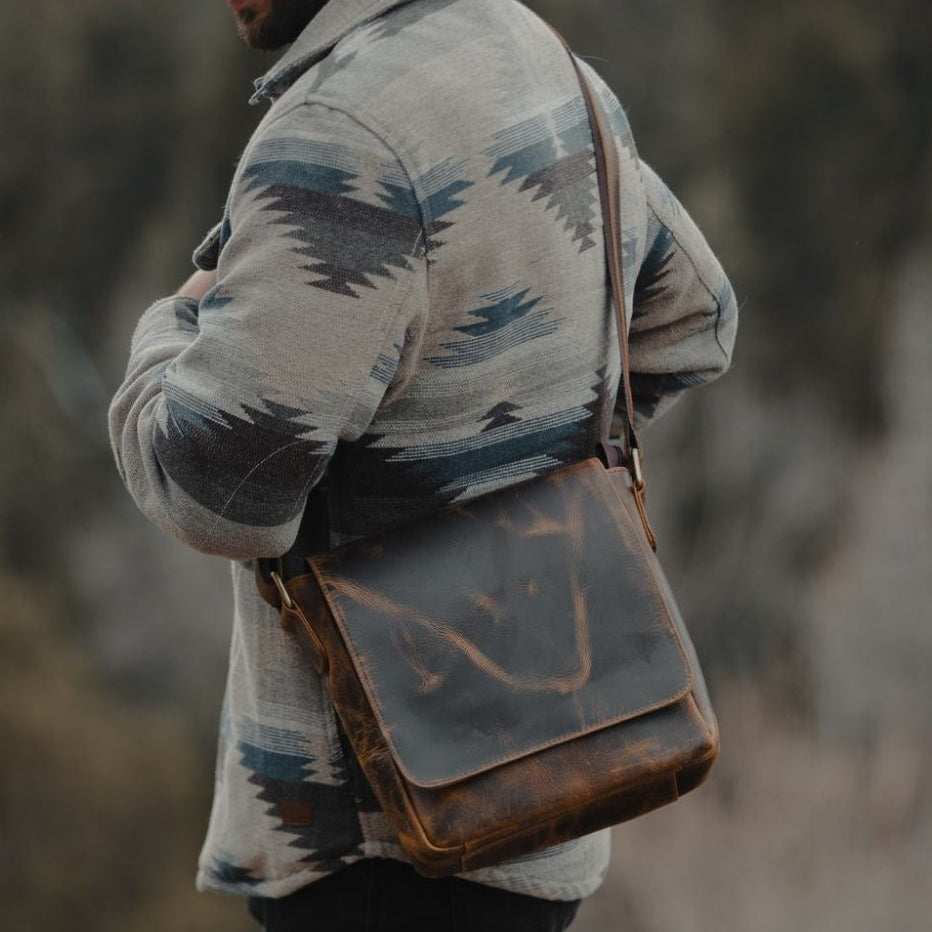 Person wearing a patterned jacket with a leather bag in a natural setting