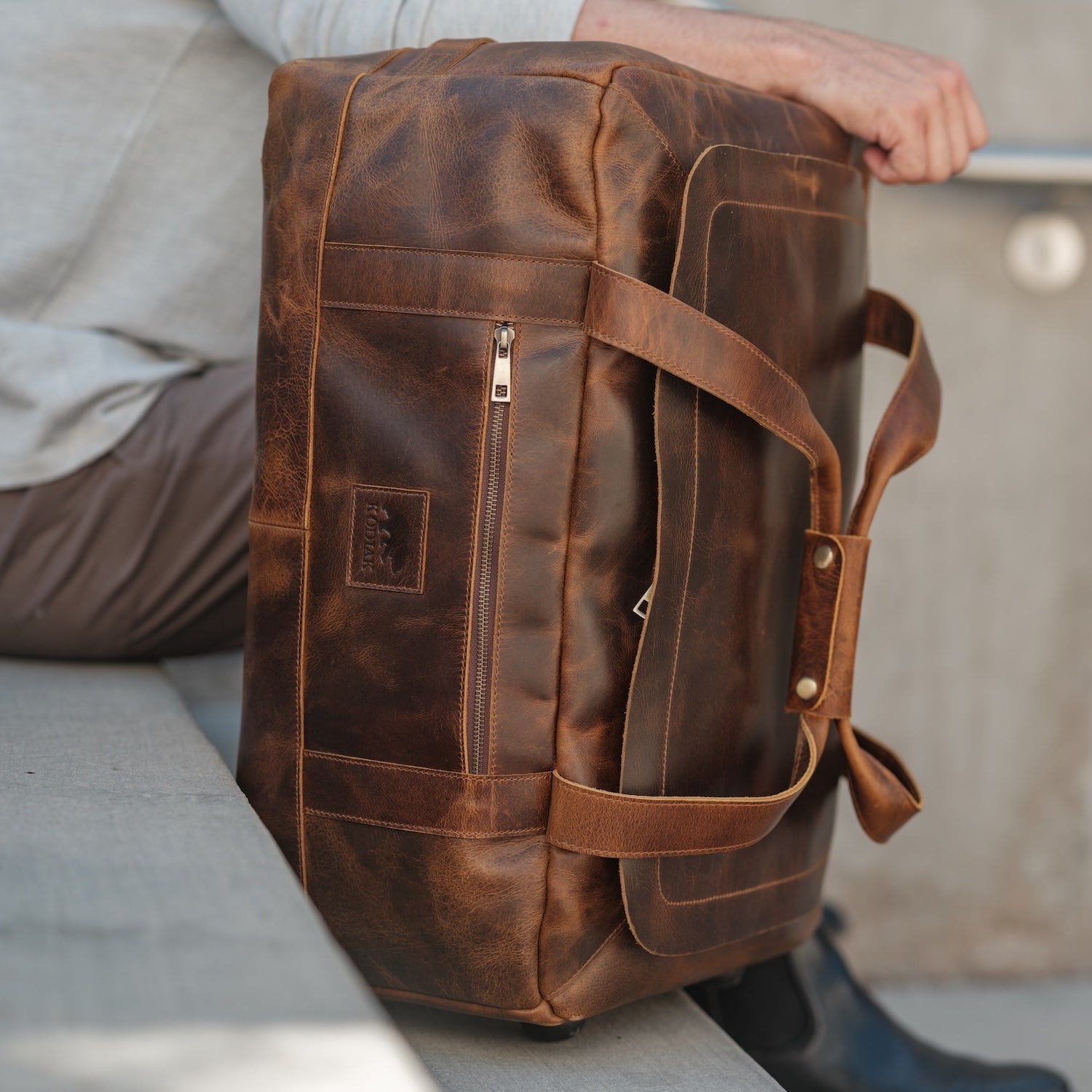 Brown leather duffel bag held by a person with a blurred background