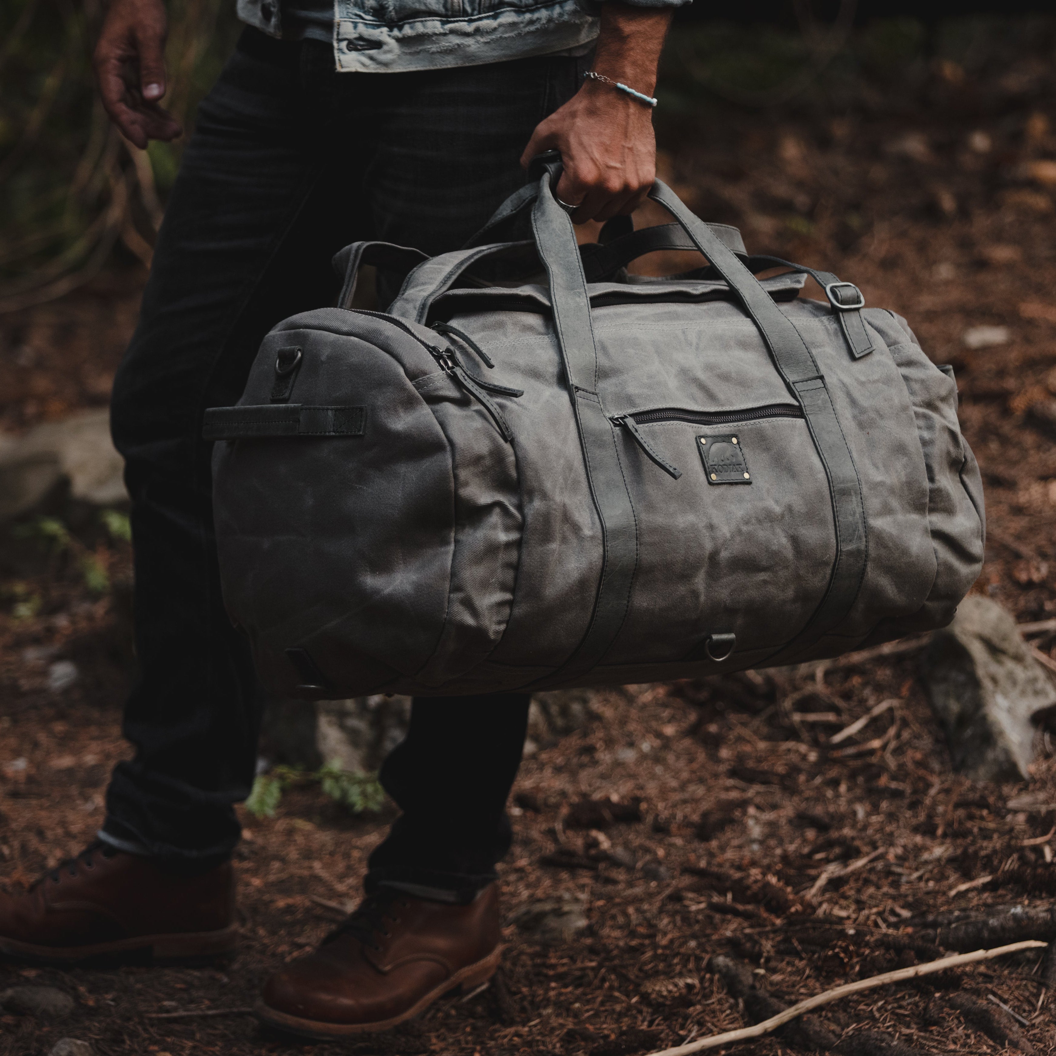 Person holding a gray duffel bag in a forest setting