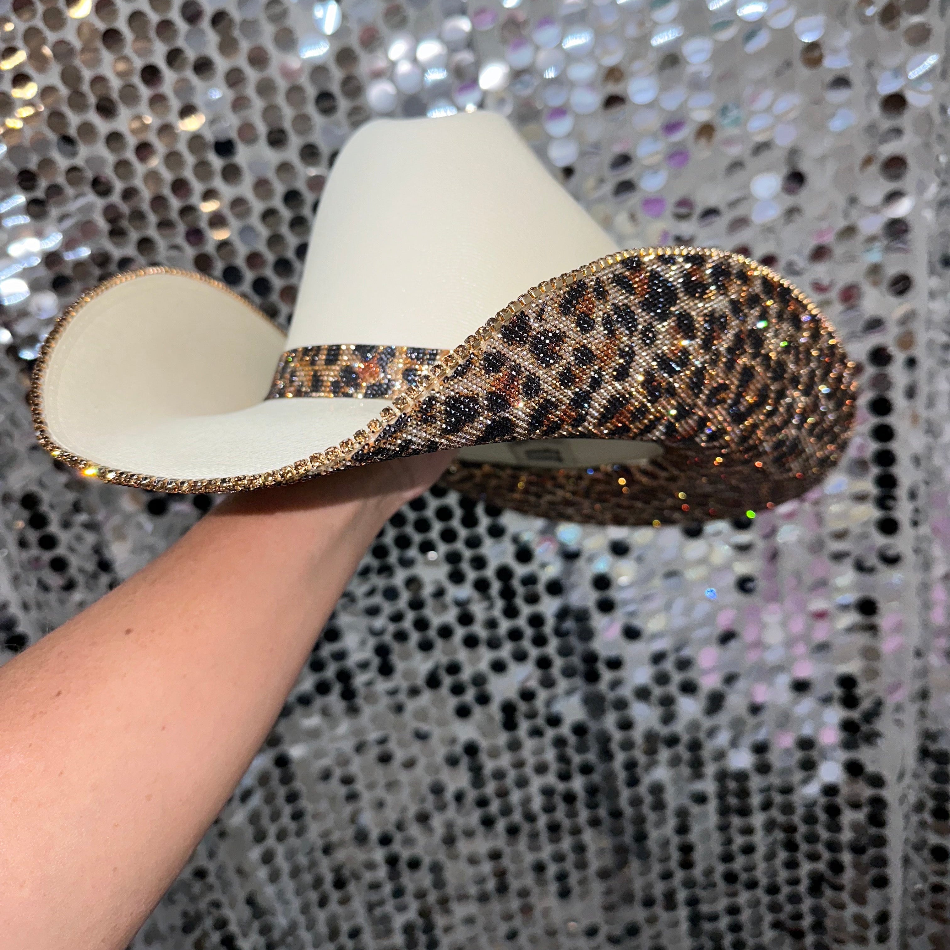 Hand holding a decorative hat with leopard print trim against a sparkling background