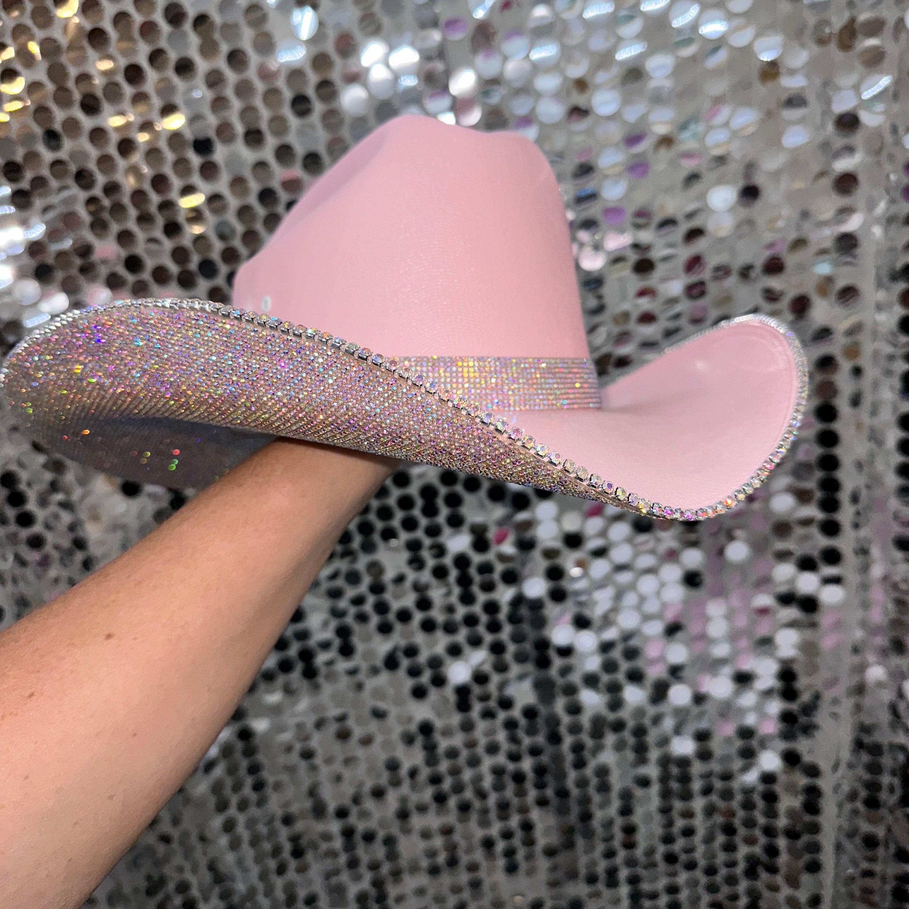 Pink hat with glittery trim held against a sequin background