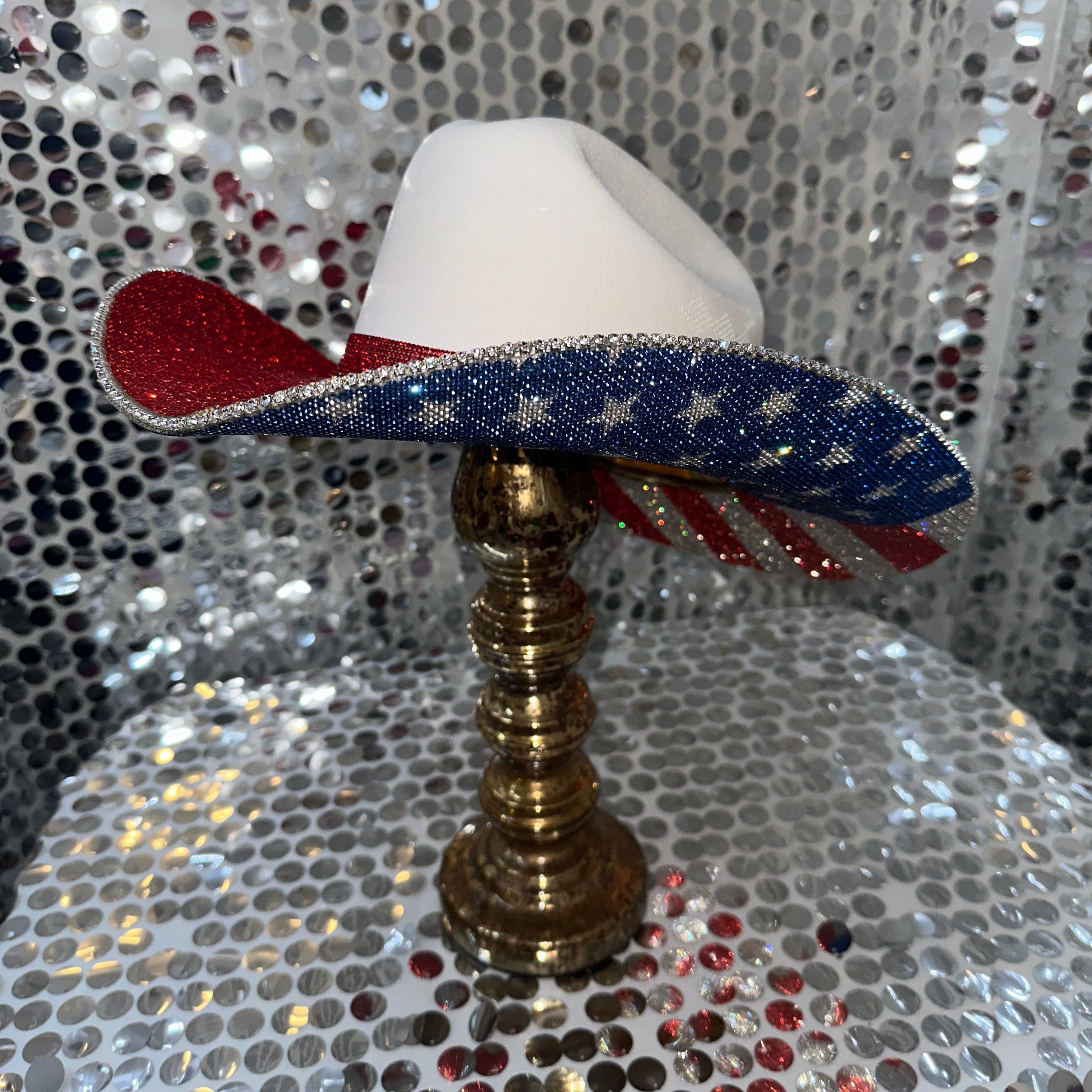 Decorative hat with American flag design on a stand against a glittery background