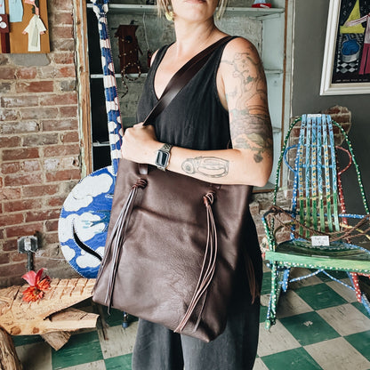 Person holding a brown leather bag in an artistic setting with colorful chairs and artwork.
