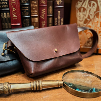 Brown leather pouch on a wooden surface with a magnifying glass and books in the background