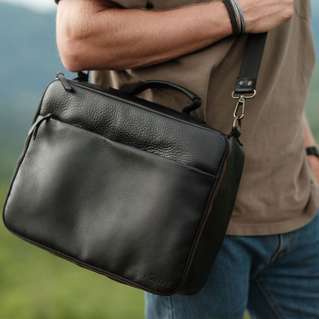 Person holding a black leather briefcase with a blurred natural background