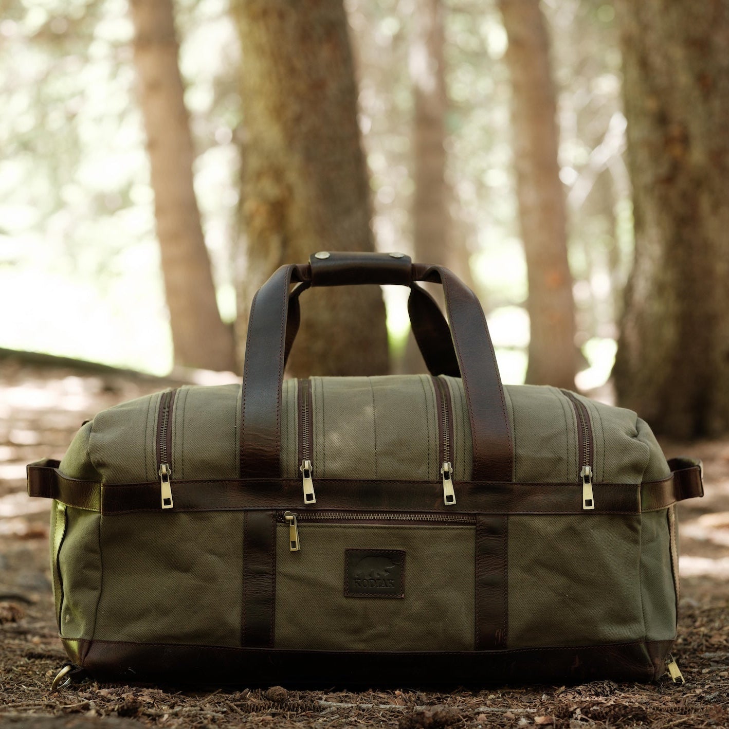 Green duffel bag with brown straps in a forest setting