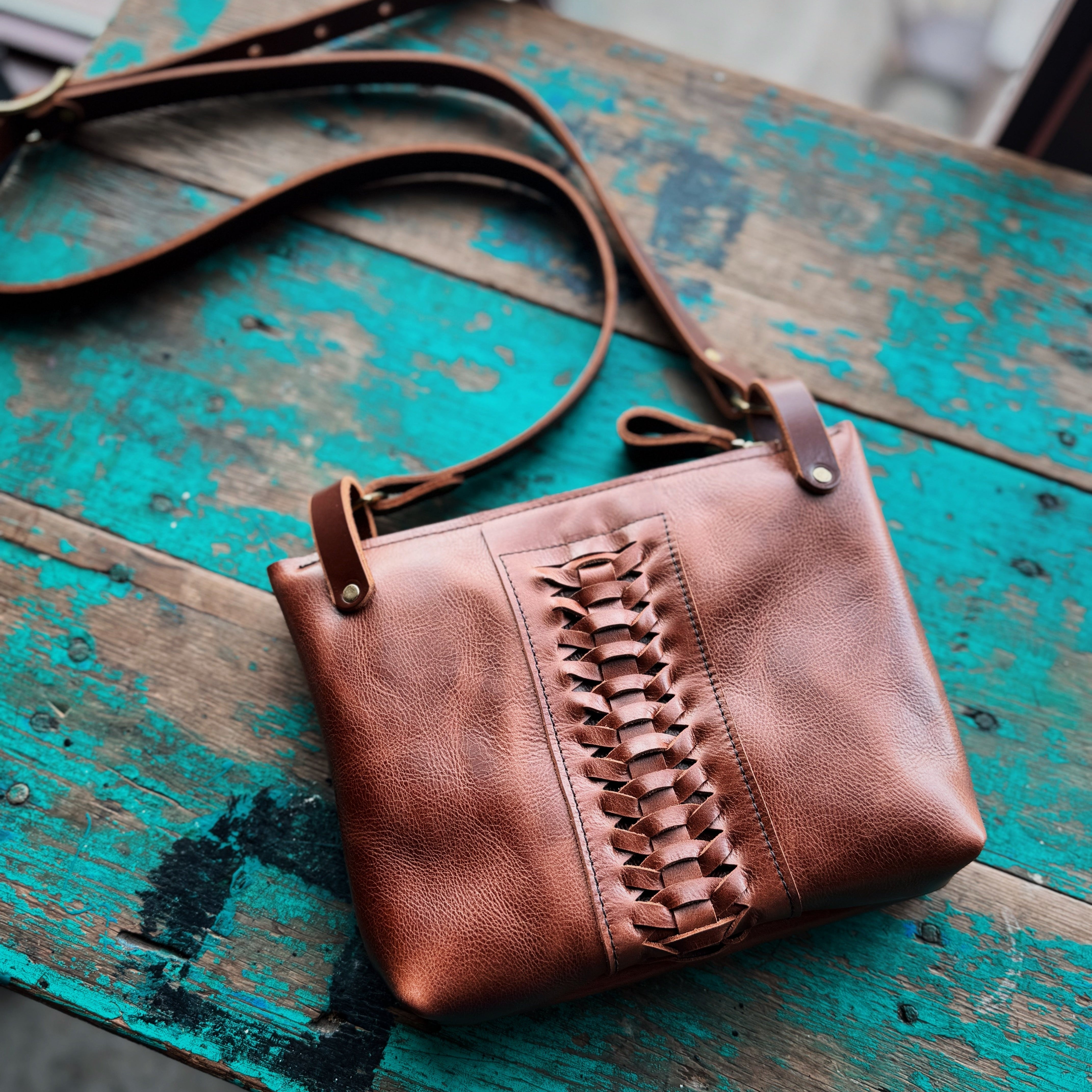 Brown leather handbag with fringe details on a rustic wooden surface