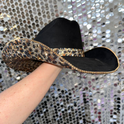 Black hat with gold sequins held by a hand against a sparkling background