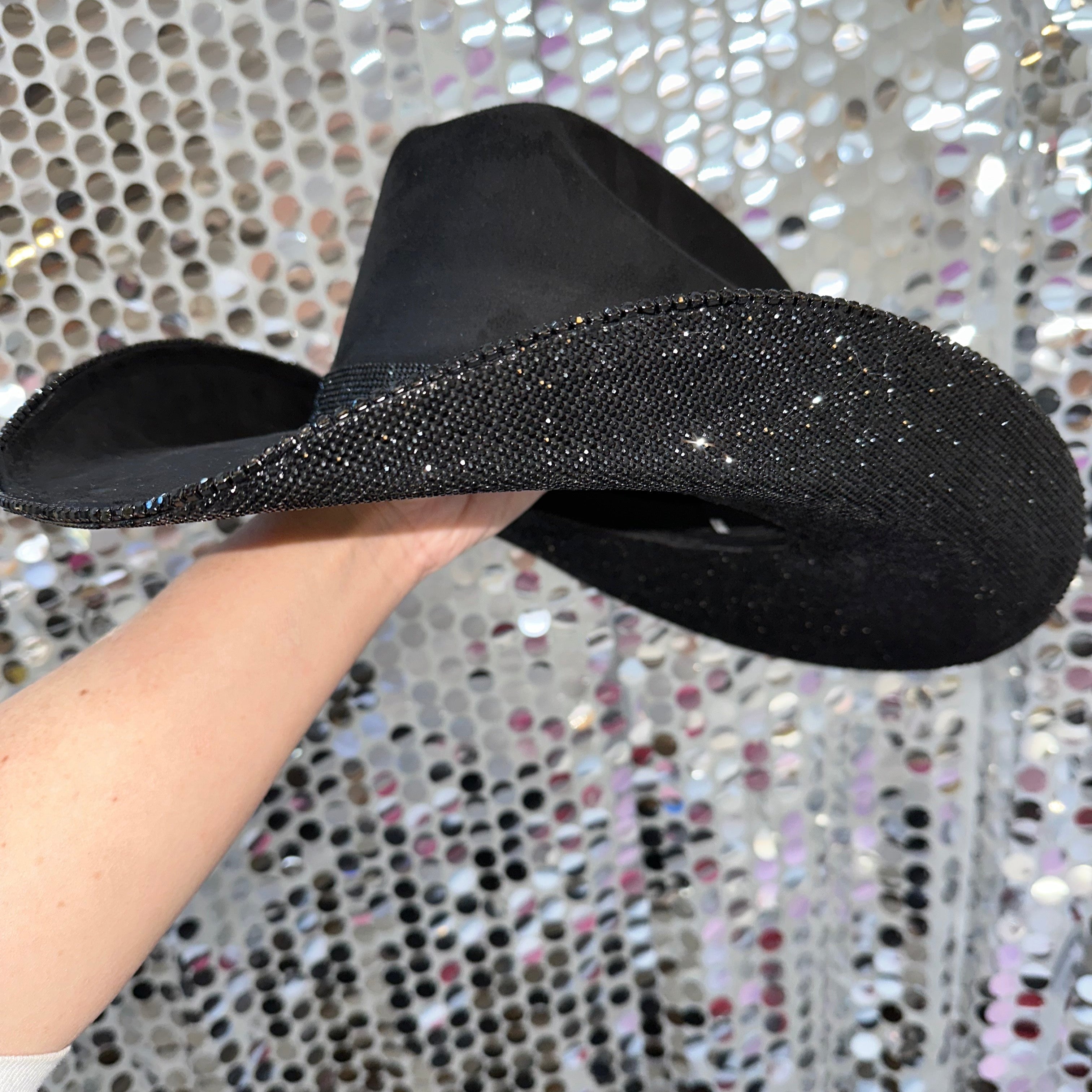 Black flat sandal with glittery sole held against a sparkling background