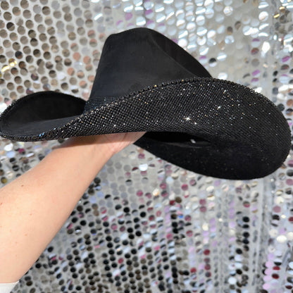 Black flat sandal with glittery sole held against a sparkling background