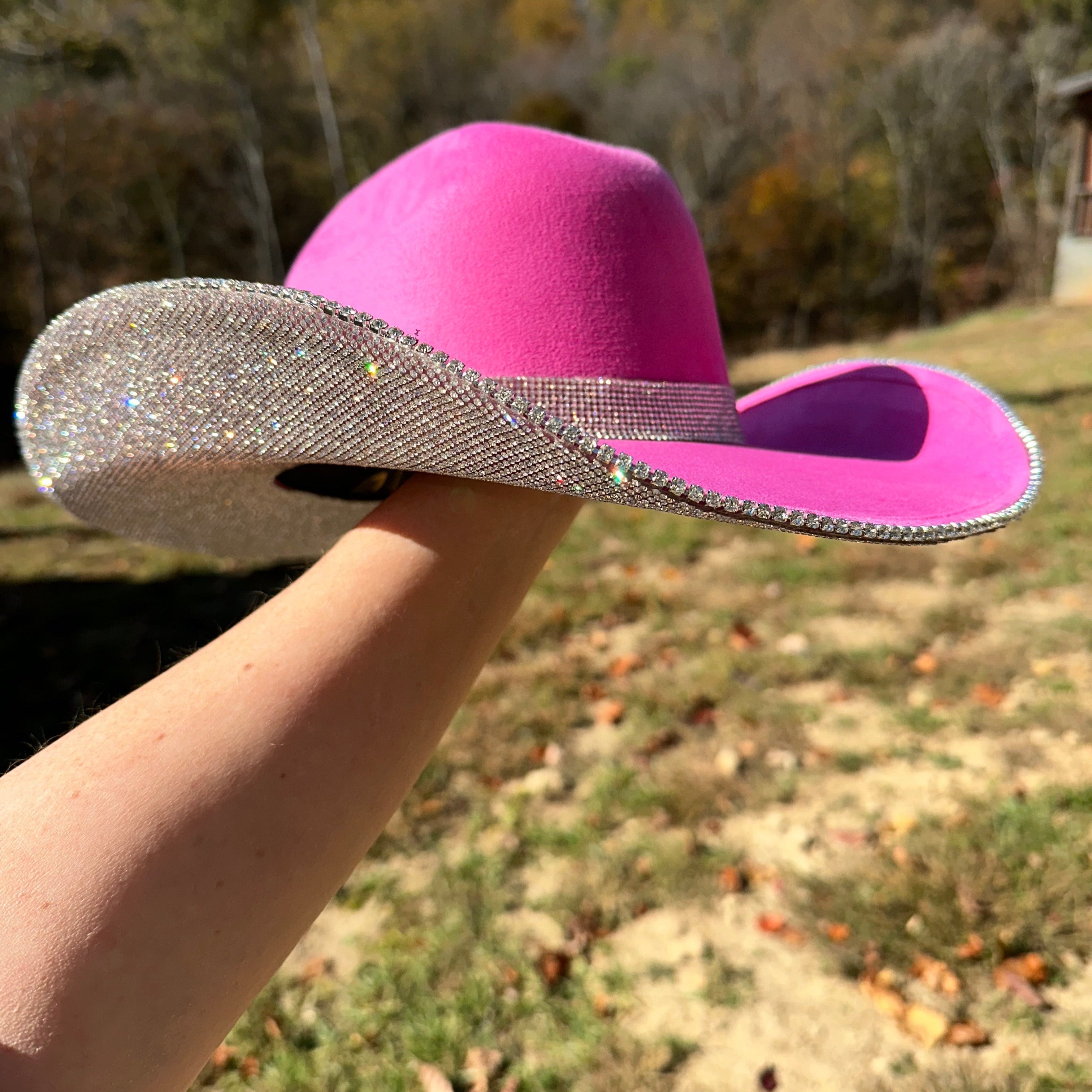 Pink cowboy hat with a silver band held by a person outdoors.