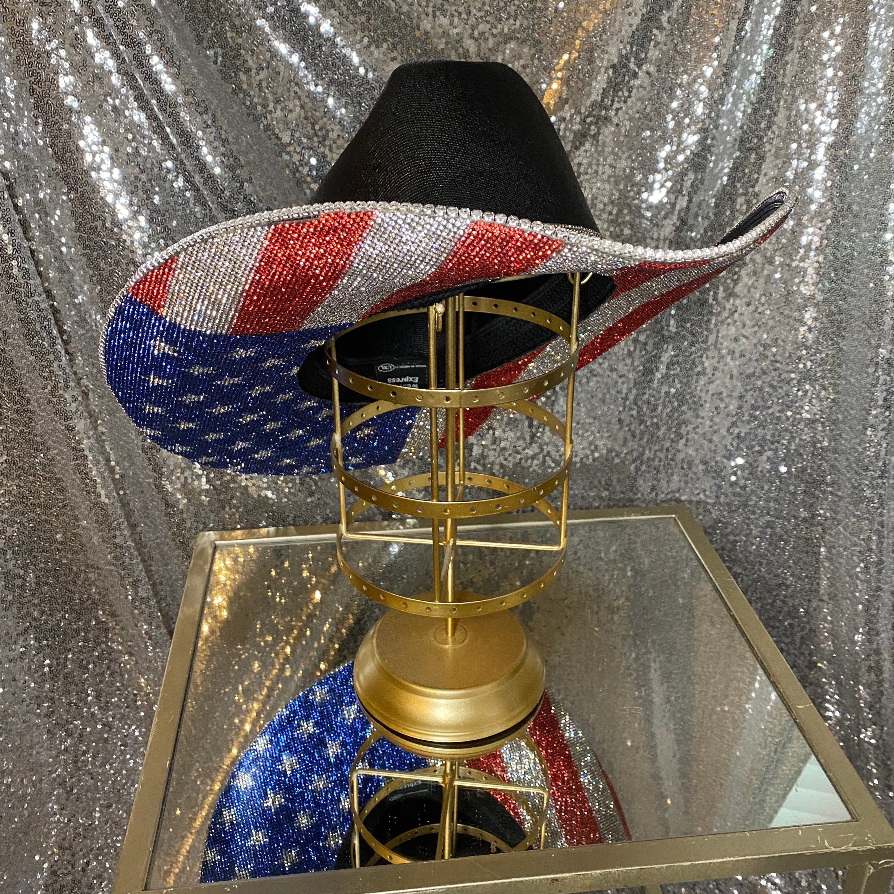 Black and red, white, and blue sequin hat on a gold stand against a silver sequin background