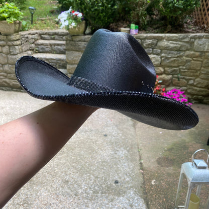 Black cowboy hat held by a person outdoors with a garden background