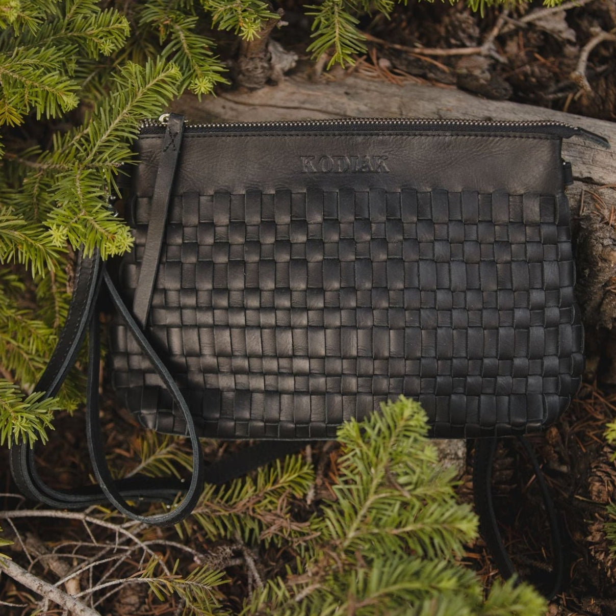 Black rectangular pouch with textured surface on a forest floor