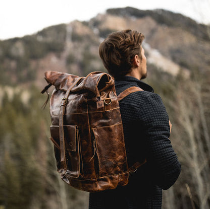 Person with a brown backpack standing in a forest with mountains in the background