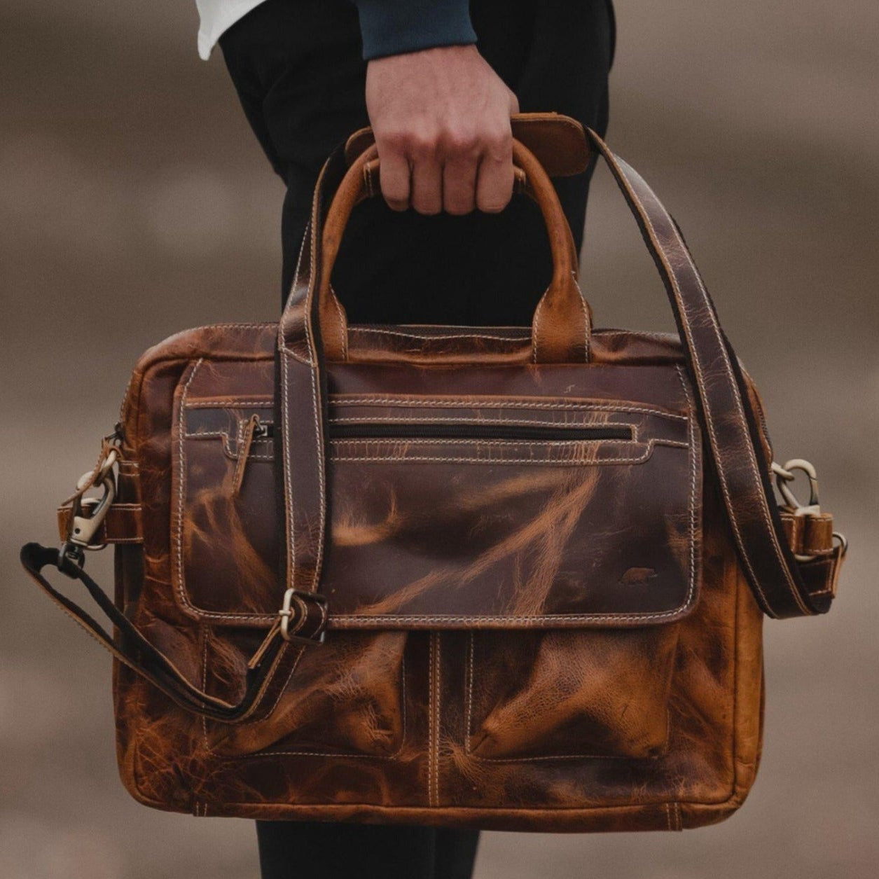 Brown leather briefcase held by a person against a blurred background