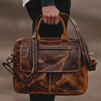 Brown leather briefcase held by a person against a blurred background